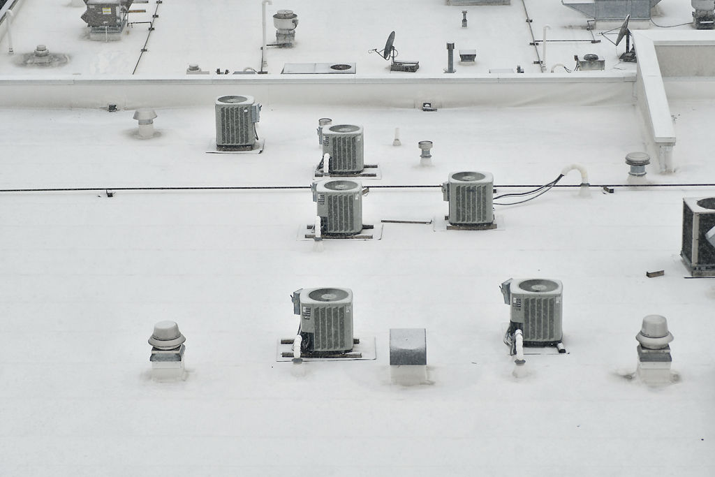 A roof full of heating and cooling units is covered with snow